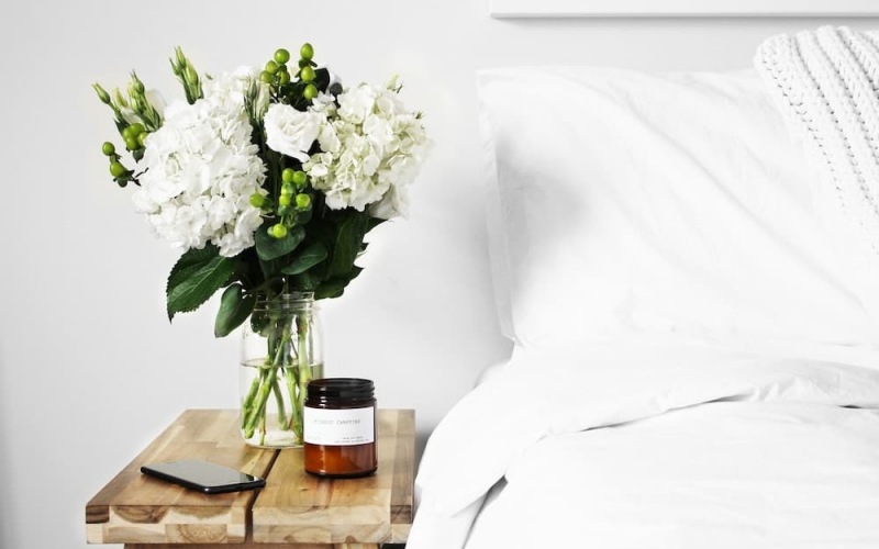 foliage and a candle beside a bed in a bright bedroom